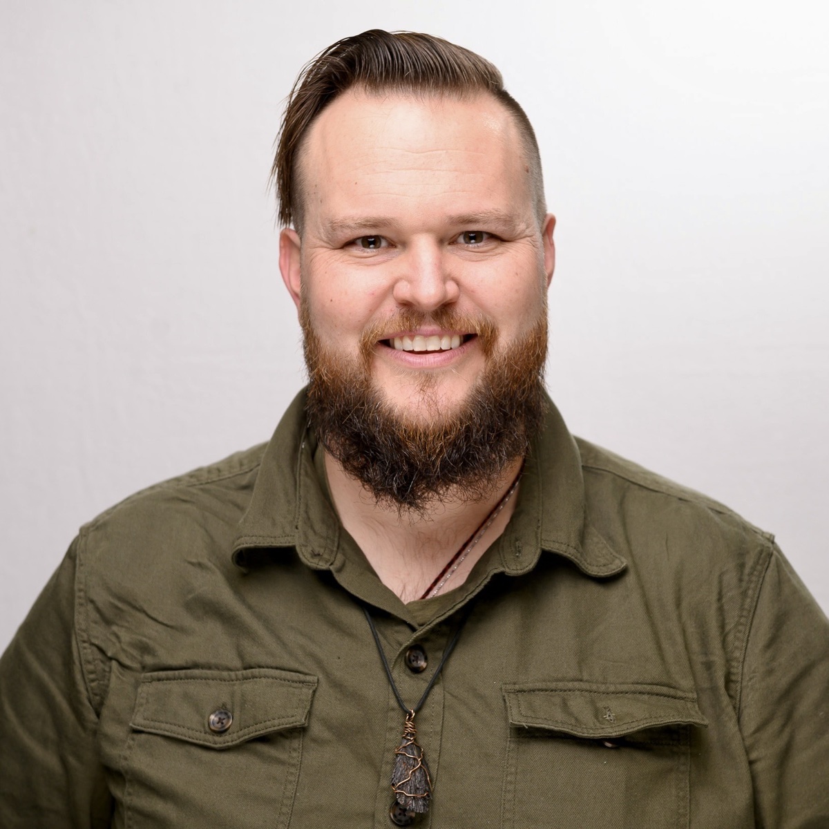 Ally Madrone, a smiling bearded man in an olive button-up shirt wearing a wire-wrapped stone pendant